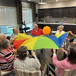 Seniors at Charter Senior Living of Hopkinsville in Hopkinsville, KY, enjoying a group activity using a parachute to keep a balloon in the air, promoting fun and social engagement in assisted living and memory care.