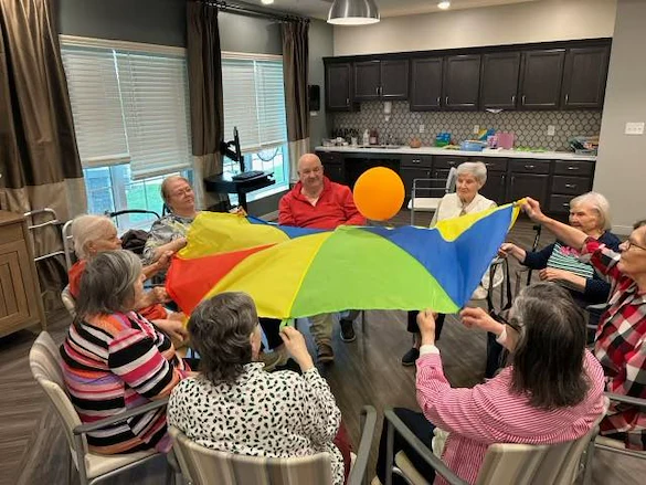 Seniors at Charter Senior Living of Hopkinsville in Hopkinsville, KY, enjoying a group activity using a parachute to keep a balloon in the air, promoting fun and social engagement in assisted living and memory care.