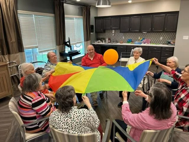 Seniors at Charter Senior Living of Hopkinsville in Hopkinsville, KY, enjoying a group activity using a parachute to keep a balloon in the air, promoting fun and social engagement in assisted living and memory care.