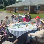 Seniors at Charter Senior Living of Hermitage in Hermitage, TN, dining together outdoors at tables, enjoying pleasant weather and socializing in independent living, assisted living, and memory care.