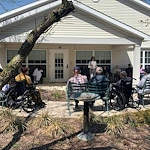 Residents at Charter Senior Living of Hazel Crest in Hazel Crest, IL, gathered outdoors as someone reads aloud, enjoying a peaceful moment and shared engagement in assisted living and memory care.