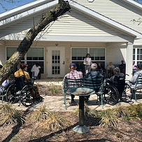 Residents at Charter Senior Living of Hazel Crest in Hazel Crest, IL, gathered outdoors as someone reads aloud, enjoying a peaceful moment and shared engagement in assisted living and memory care.