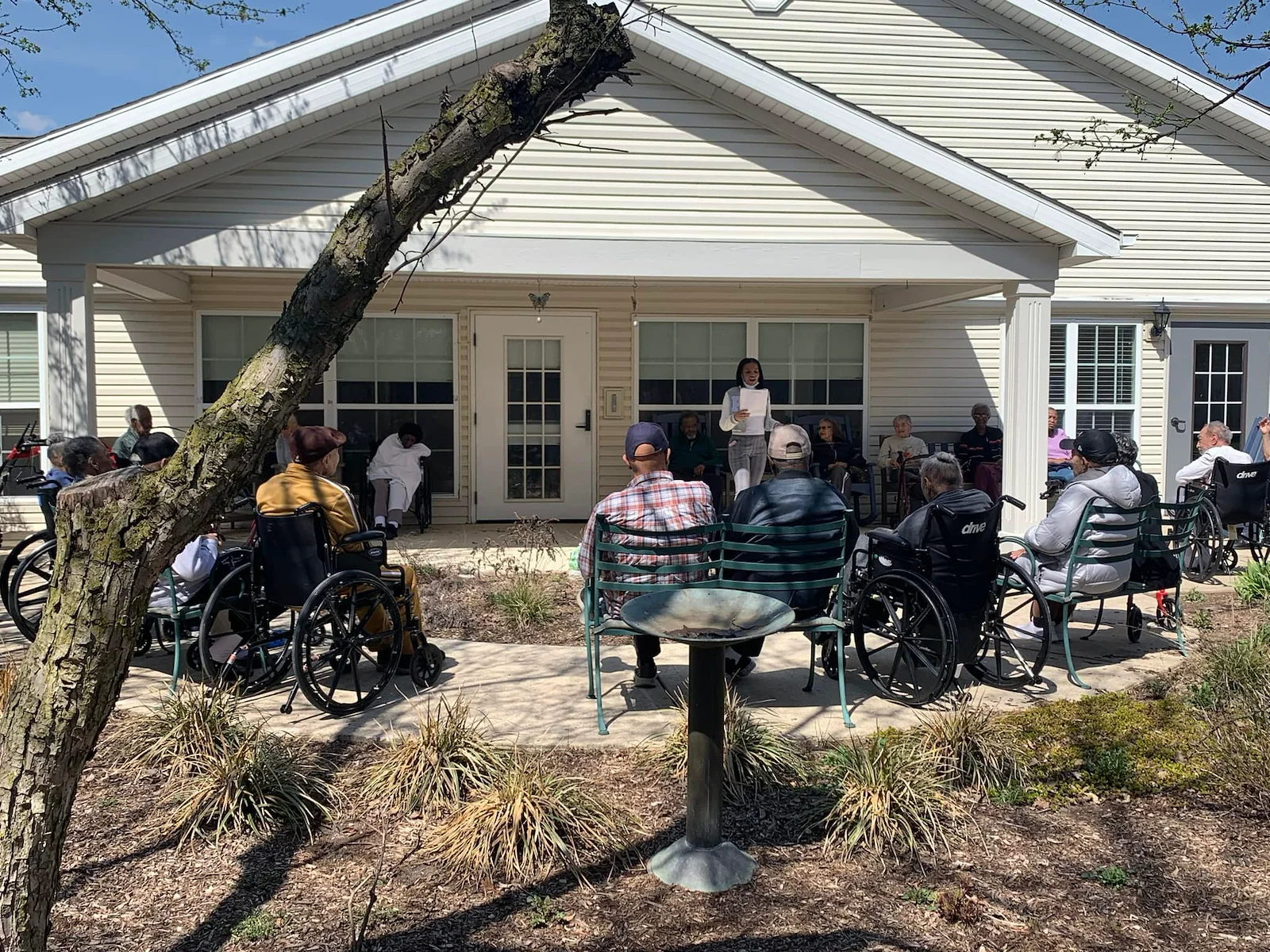 Residents at Charter Senior Living of Hazel Crest in Hazel Crest, IL, gathered outdoors as someone reads aloud, enjoying a peaceful moment and shared engagement in assisted living and memory care.