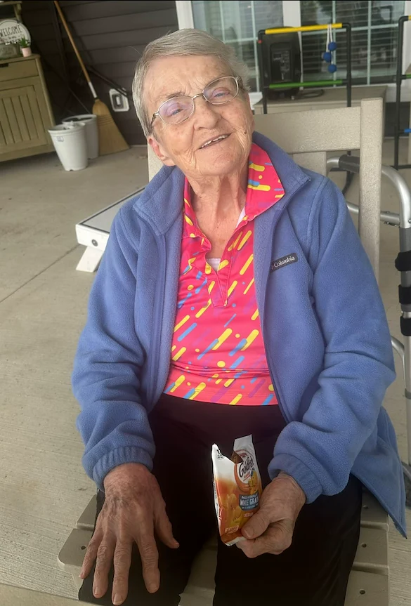 Smiling resident at Charter Senior Living of Hopkinsville in Hopkinsville, KY, enjoying Goldfish crackers outside, promoting happiness and wellness in assisted living and memory care.