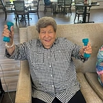 Senior woman smiling and holding weights during an exercise class at Charter Senior Living of Hermitage in Hermitage, TN, promoting fitness and wellness in independent living, assisted living, and memory care.