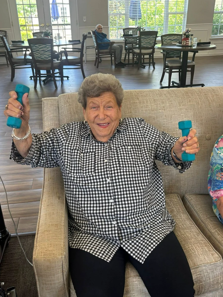 Senior woman smiling and holding weights during an exercise class at Charter Senior Living of Hermitage in Hermitage, TN, promoting fitness and wellness in independent living, assisted living, and memory care.