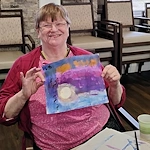 American House Westland Venoy senior living community offering independent living, assisted living, and respite care in Westland, MI, resident smiling as she shows her art creation