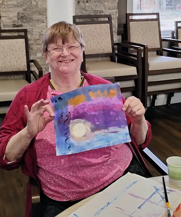 American House Westland Venoy senior living community offering independent living, assisted living, and respite care in Westland, MI, resident smiling as she shows her art creation