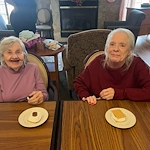 Two seniors in assisted living at Charter Senior Living of Hasmer Lake in Jackson, WI, smiling and enjoying a sweet treat together, highlighting community and comfort.