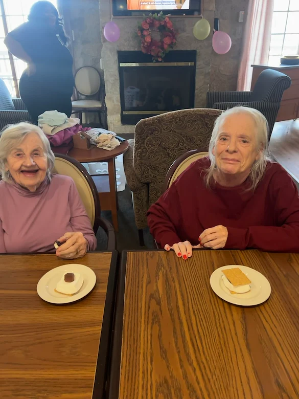 Two seniors in assisted living at Charter Senior Living of Hasmer Lake in Jackson, WI, smiling and enjoying a sweet treat together, highlighting community and comfort.