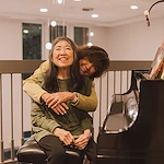 woman embracing another next to piano