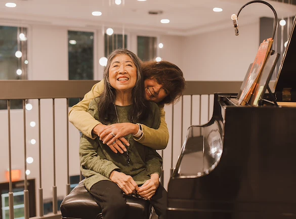 woman embracing another next to piano