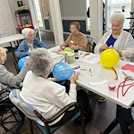 Seniors at Charter Senior Living of Jackson in Jackson, TN, gathered around a table in a well-lit room, enjoying a craft activity and socializing, fostering creativity and community in assisted living and memory care.