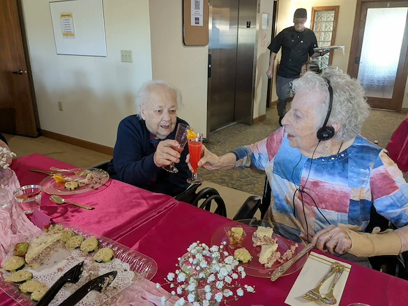 Seniors in assisted living and memory care at Charter Senior Living of Hasmer Lake in Jackson, WI, cheering with drinks and enjoying snacks together, fostering community and celebration
