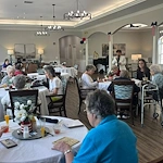 Seniors at Charter Senior Living of Hermitage in Hermitage, TN, playing Bingo together and enjoying refreshing drinks in a well-lit common area, promoting social engagement in independent living, assisted living, and memory care.