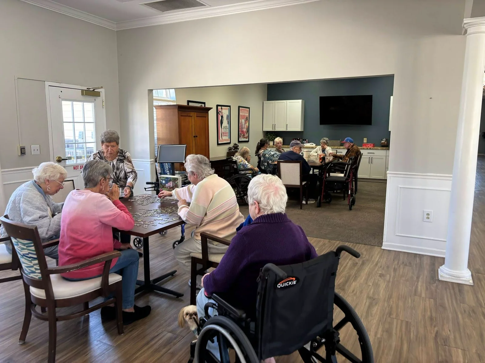 Two groups of seniors at Charter Senior Living of Hermitage in Hermitage, TN, gathered in a common area, with one group working on a puzzle and another socializing, fostering community and engagement in independent living, assisted living, and memory care.