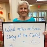 The Oaks Gracious Retirement Living Hawthorn Senior Independent Living in Georgetown, Texas resident holding a sign that says "What makes me smile: living at The Oaks!"