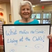 The Oaks Gracious Retirement Living Hawthorn Senior Independent Living in Georgetown, Texas resident holding a sign that says "What makes me smile: living at The Oaks!"