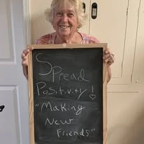Providence Meadows Gracious Retirement Living Hawthorn Senior Independent Living in Charlotte, North Carolina resident holding a sign that says "spread positivity! Making new friends"