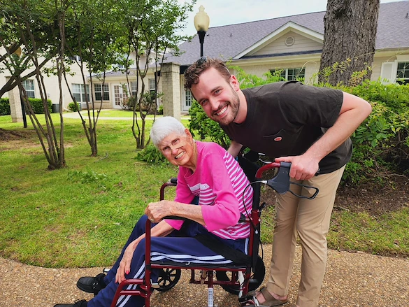 The Chateaus at Montclair Senior Memory Care in Shreveport, LA resident in a wheelchair being pushed by a staff member
