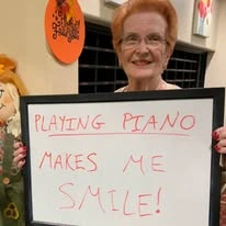 Providence Meadows Gracious Retirement Living Hawthorn Senior Independent Living in Charlotte, North Carolina resident holding a sign that says "playing piano makes me smile!"