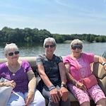 Three senior women residents from Charter Senior Living of Hermitage in Hermitage, TN, smiling and enjoying sunshine on a boat outing, promoting active and social lifestyles in independent living, assisted living, and memory care.