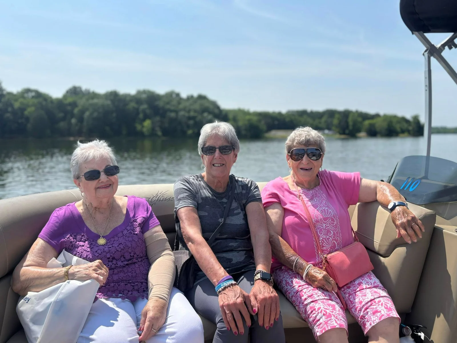 Three senior women residents from Charter Senior Living of Hermitage in Hermitage, TN, smiling and enjoying sunshine on a boat outing, promoting active and social lifestyles in independent living, assisted living, and memory care.