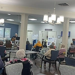 Seniors at Charter Senior Living of Jackson in Jackson, TN, gathered in a common area enjoying live music with singing and guitar playing, fostering social engagement in assisted living and memory care.