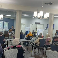 Seniors at Charter Senior Living of Jackson in Jackson, TN, gathered in a common area enjoying live music with singing and guitar playing, fostering social engagement in assisted living and memory care.