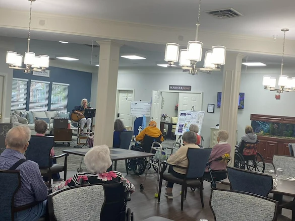 Seniors at Charter Senior Living of Jackson in Jackson, TN, gathered in a common area enjoying live music with singing and guitar playing, fostering social engagement in assisted living and memory care.