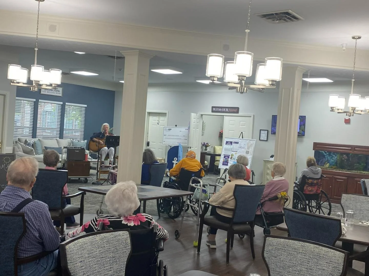 Seniors at Charter Senior Living of Jackson in Jackson, TN, gathered in a common area enjoying live music with singing and guitar playing, fostering social engagement in assisted living and memory care.