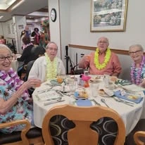 Ascension Living Bethlehem Woods Village senior living community offering independent living, assisted living, and memory care in La Grange Park, IL, residents enjoying dining together and socializing at a Hawaiian-themed dinner event