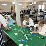 Three seniors gathered around a table playing blackjack with a staff member acting as dealer in the dining room at Charter Senior Living of Jackson in Jackson, TN, enjoying a fun, mentally engaging activity in assisted living and memory care.