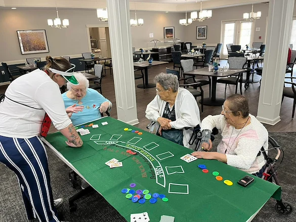 Three seniors gathered around a table playing blackjack with a staff member acting as dealer in the dining room at Charter Senior Living of Jackson in Jackson, TN, enjoying a fun, mentally engaging activity in assisted living and memory care.
