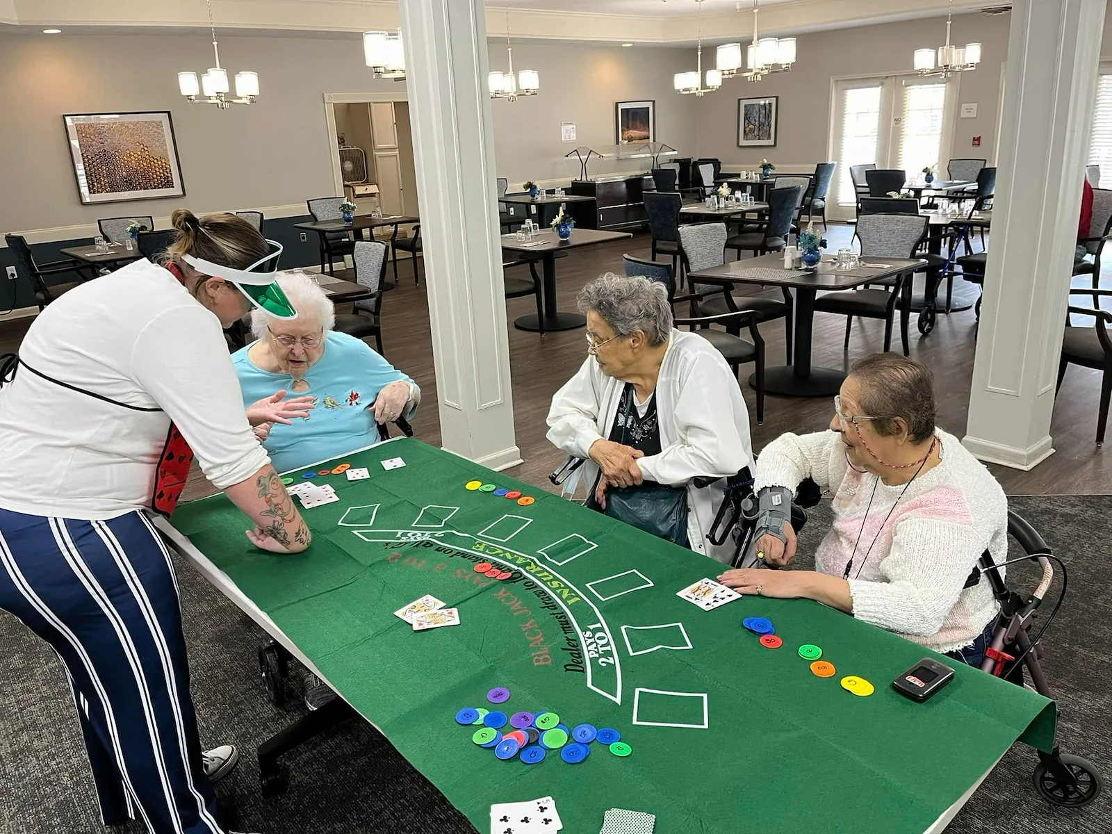 Three seniors gathered around a table playing blackjack with a staff member acting as dealer in the dining room at Charter Senior Living of Jackson in Jackson, TN, enjoying a fun, mentally engaging activity in assisted living and memory care.