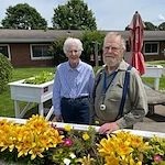Wesley Manor Assisted Living Community offering assisted living and continuing care retirement community (CCRC) services in Louisville, KY, smiling residents standing by a flowerbed outside