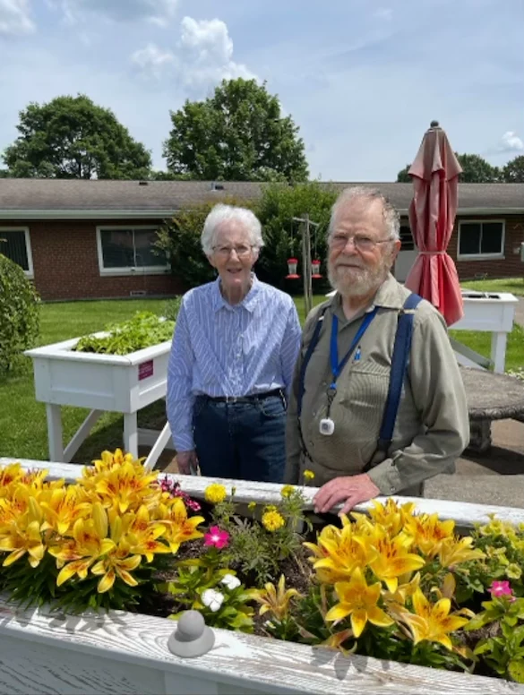 Wesley Manor Assisted Living Community offering assisted living and continuing care retirement community (CCRC) services in Louisville, KY, smiling residents standing by a flowerbed outside