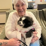 Park Vista Retirement Living - Camanche, IA, resident smiles with a visiting dog