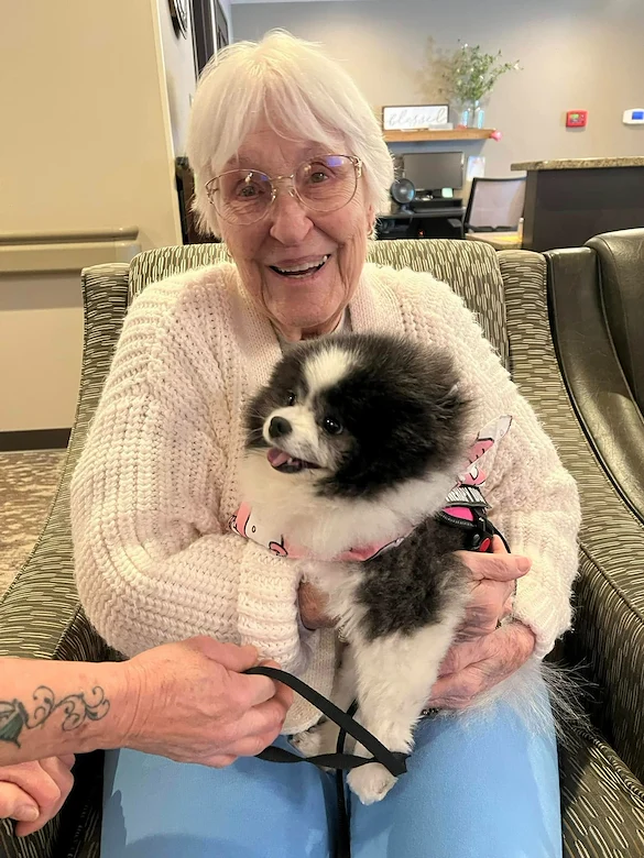 Park Vista Retirement Living - Camanche, IA, resident smiles with a visiting dog