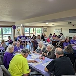 Seniors in assisted living and memory care at Charter Senior Living of Hasmer Lake in Jackson, WI, gathered for a fun community Bingo event, with vibrant purple decor enhancing the lively atmosphere.