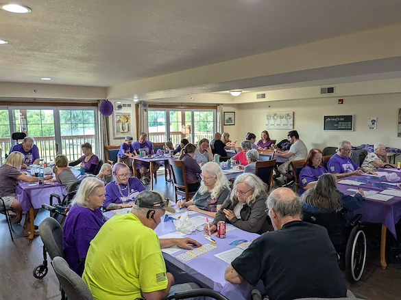 Seniors in assisted living and memory care at Charter Senior Living of Hasmer Lake in Jackson, WI, gathered for a fun community Bingo event, with vibrant purple decor enhancing the lively atmosphere.