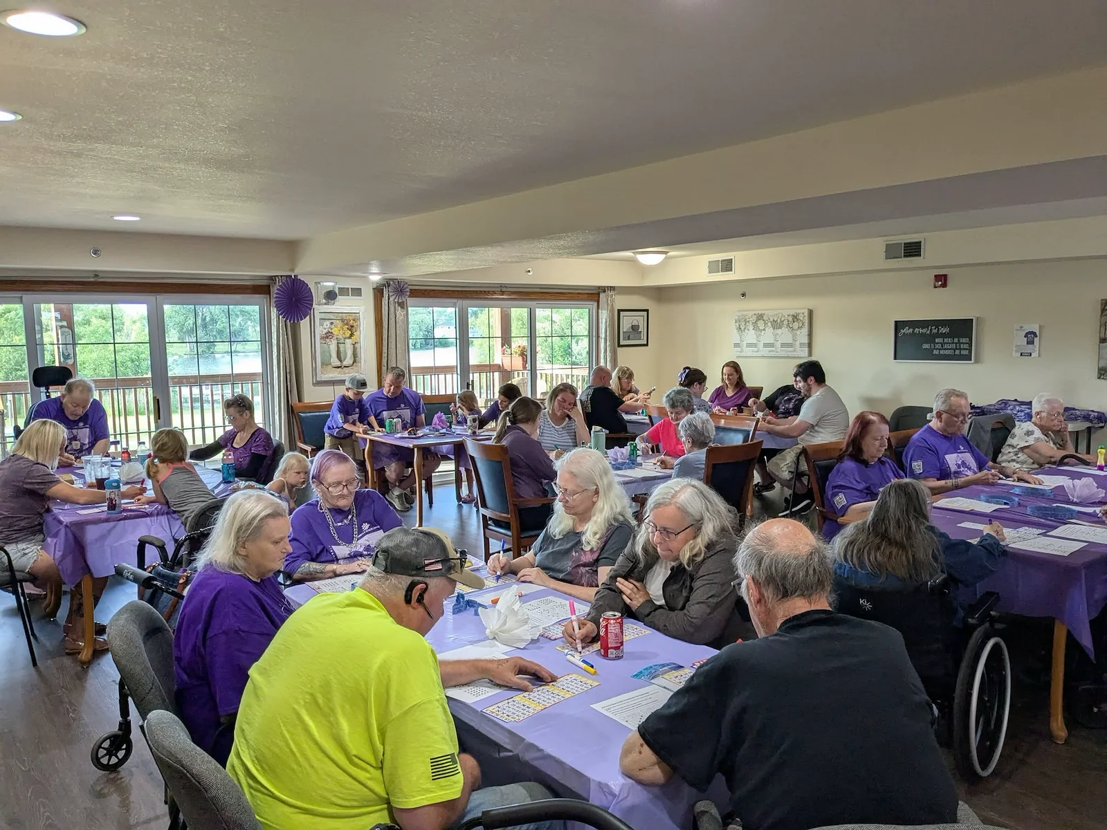 Seniors in assisted living and memory care at Charter Senior Living of Hasmer Lake in Jackson, WI, gathered for a fun community Bingo event, with vibrant purple decor enhancing the lively atmosphere.