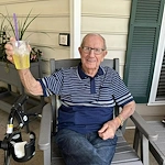 Happy senior man sitting outside in a chair by the building at Charter Senior Living of Jackson in Jackson, TN, holding up a drink and enjoying a relaxed moment in assisted living and memory care.