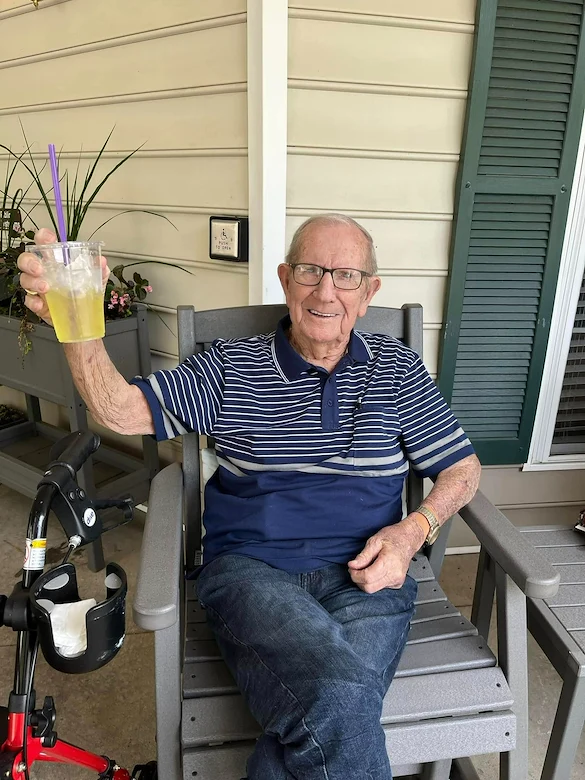 Happy senior man sitting outside in a chair by the building at Charter Senior Living of Jackson in Jackson, TN, holding up a drink and enjoying a relaxed moment in assisted living and memory care.