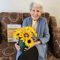 Alexis Estates Gracious Retirement Living by Hawthorn Senior Living, independent living in Allen, TX, resident smiling with a bouquet of sunflowers