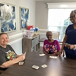 Residents at Charter Senior Living of Hazel Crest in Hazel Crest, IL, playing cards with a nurse in a bright, naturally lit common area, fostering connection, fun, and engagement in assisted living and memory care.