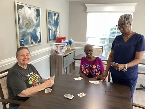 Residents at Charter Senior Living of Hazel Crest in Hazel Crest, IL, playing cards with a nurse in a bright, naturally lit common area, fostering connection, fun, and engagement in assisted living and memory care.