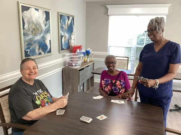 Residents at Charter Senior Living of Hazel Crest in Hazel Crest, IL, playing cards with a nurse in a bright, naturally lit common area, fostering connection, fun, and engagement in assisted living and memory care.