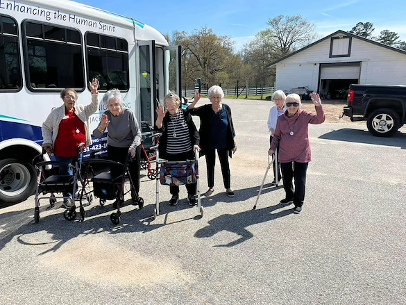 Seniors from Charter Senior Living of Jackson in Jackson, TN, smiling and waving outside a community van during an off-site trip on a sunny day, with a barn in the background, promoting social engagement and active lifestyles in assisted living and memory care.