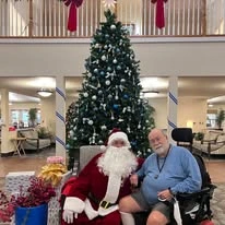 Wenatchee Senior Living by Cogir senior living community offering independent living, assisted living, and respite care in Wenatchee, WA, resident with Santa Claus by the Christmas tree in the community lobby